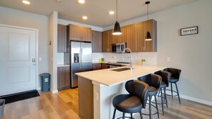 A modern kitchen with wooden cabinets, stainless steel appliances, a central island with bar stools, and pendant lighting. - Pool Access! Luxe Condo 7 Mi to Coquina Beach (Bradenton)