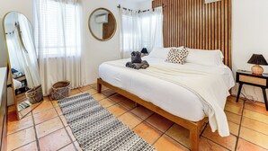 Un dormitorio con cama de madera, ropa de cama blanca, un espejo redondo y un ventilador de techo.