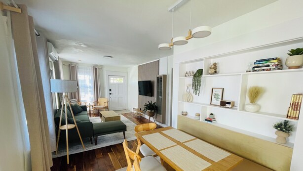 Una sala de estar moderna con una mesa de comedor de madera, un sofá y un televisor montado en la pared.