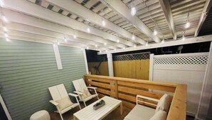 Un patio al aire libre con piso de madera, muebles blancos y luces colgantes.