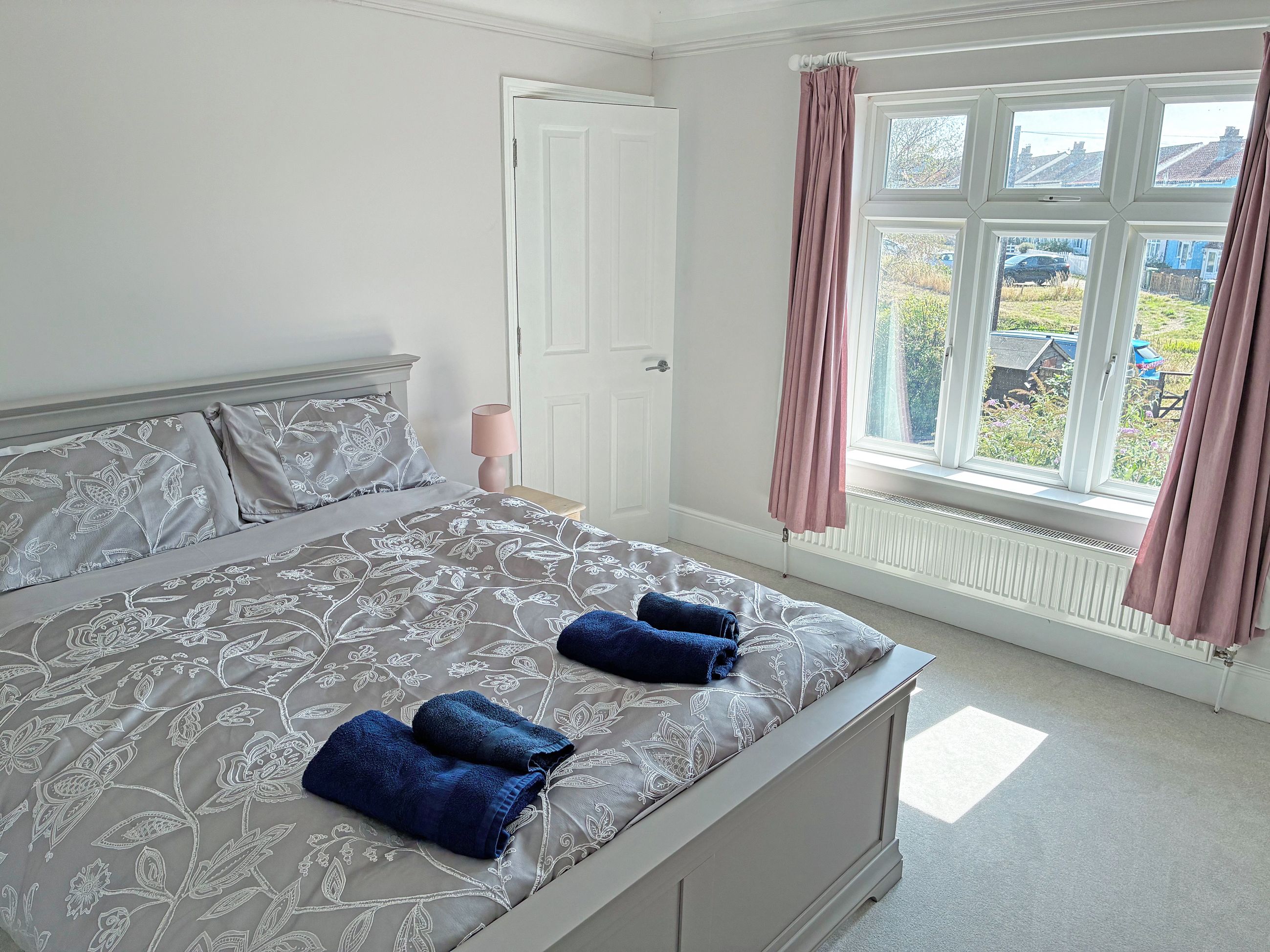 A bedroom with a bed, a nightstand, a window with curtains, and a view of the outside.