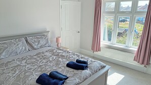 A bedroom with a bed, a nightstand, a window with curtains, and a view of the outside. - 3 bedroom accommodation in Sheringham (Sheringham)