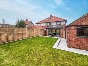A backyard with a well-maintained lawn, a wooden fence, and a brick house with a tiled roof. - 3 bedroom accommodation in Whitby (Whitby)