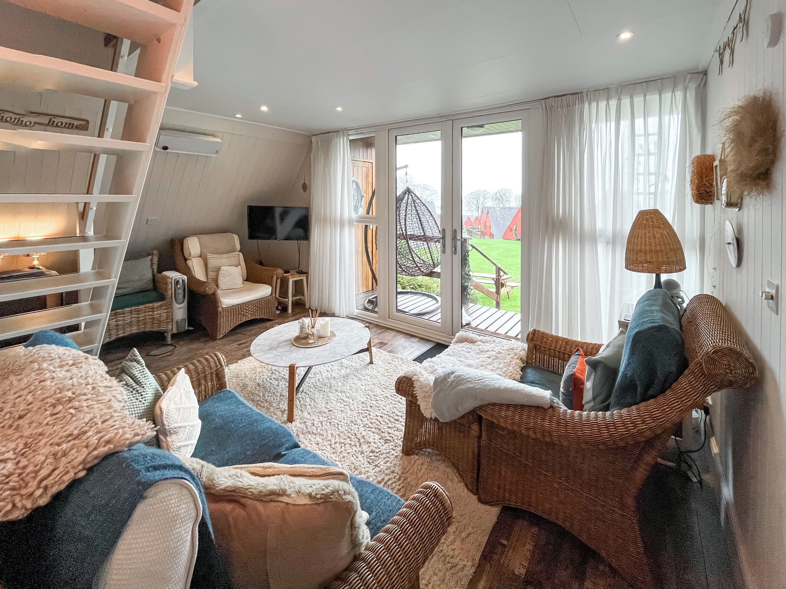 Ein gemütliches Wohnzimmer mit Korbmöbeln, einem Flachbildfernseher und Blick ins Freie.