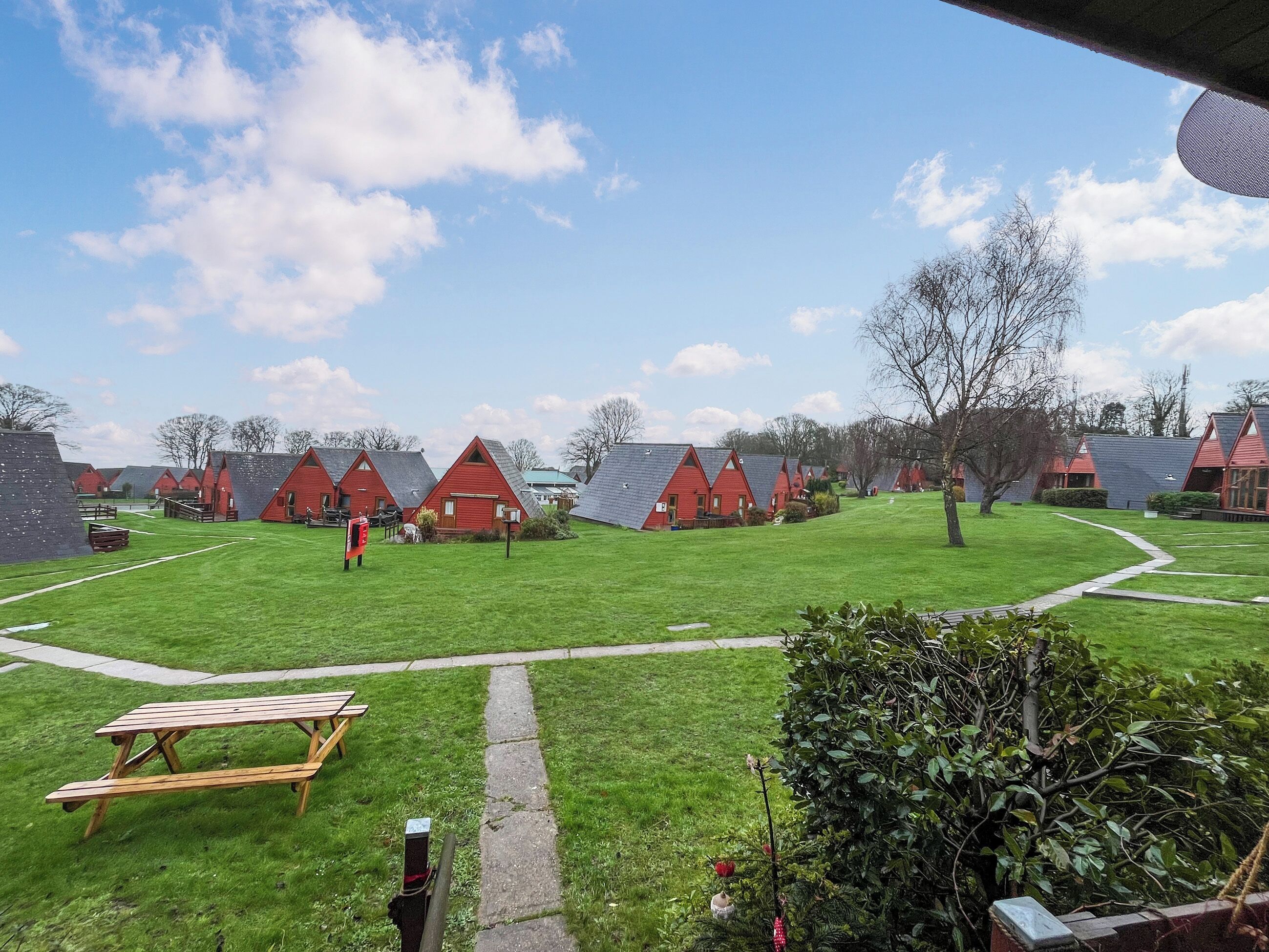A row of red-roofed cabins with a grassy lawn and picnic table in the foreground.
