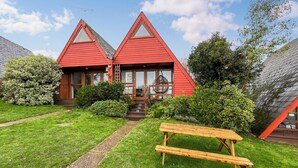 Et rødt hus med to etager, en træterrasse og et picnicbord i forhaven.