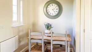 Ein Essbereich mit Holztisch und Stühlen, einer Wanduhr und einem Blumentopf.