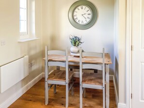 A dining area with a wooden table and chairs, a wall clock, and a potted plant. - 2 bedroom accommodation in Garlieston (Garlieston)