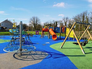 A playground with a climbing structure, a slide, and a swing set. - 2 bedroom accommodation in Garlieston (Garlieston)