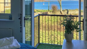Ein Zimmer mit großem Fenster, einem Bett, einer Topfpflanze und Blick aufs Meer.