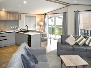 A modern living room with a grey sofa, a small wooden coffee table, and a kitchen area with a built-in sink and cabinets. - 2 bedroom accommodation in Lyme Regis (Lyme Regis)