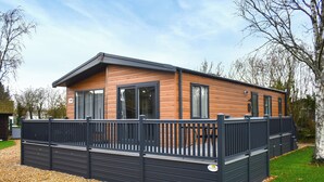 Ein modernes Mobilheim mit einer Terrasse, großen Fenstern und einem eingezäunten Außenbereich.