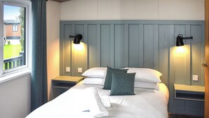 Ein ordentlich gemachtes Bett mit weißen Bettwäsche und einem gefalteten Handtuch, zwei Nachttischlampen und ein Fenster mit Vorhängen.