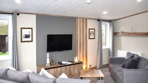 Ein modernes Wohnzimmer mit Fernseher, grauen Sofas, einem Holztisch und einem Kamin.