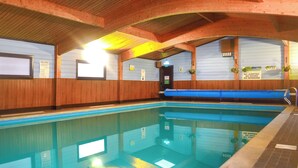 Una piscina interior amb parets de fusta, un solàrium blau i diversos senyals de seguretat.