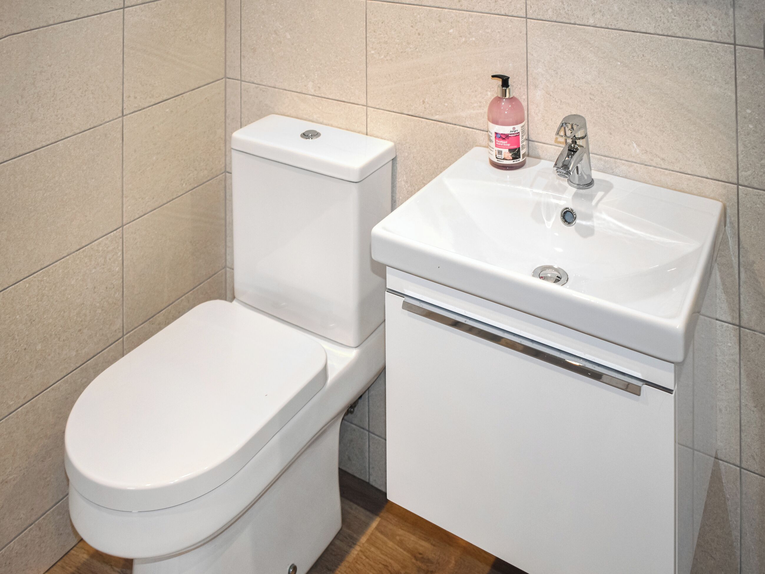 A bathroom with a white toilet, a sink, and a bottle of hand soap on the sink.