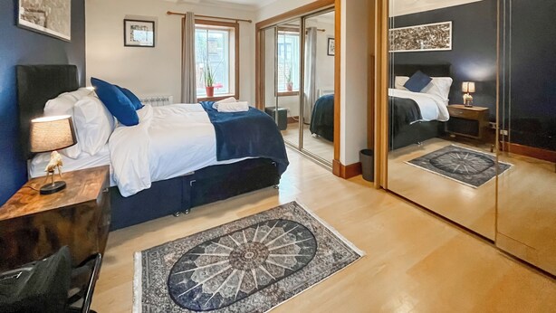Un dormitorio con cama, mesita de noche, lámpara y un espejo grande.