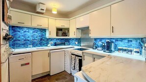 Una cocina con armarios blancos, salpicadero de azulejos azules, lavavajillas, estufa y cafetera.