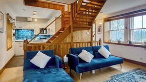 Un salón amplio con una escalera de madera, una cocina al fondo y un ventanal con vistas.