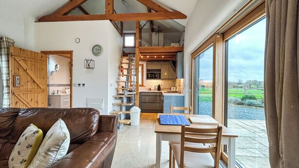 Een ruime woonkamer met een bruine leren bank, een eettafel met stoelen en een groot raam met uitzicht op de omgeving.