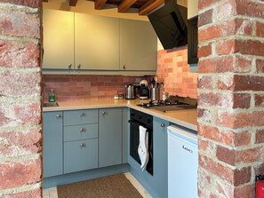 A compact kitchen with light blue cabinets, a brick backsplash, a gas stove, and a dishwasher.