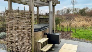 Ein rustikaler Sitzbereich im Freien mit einer Holzpergola, einer gewebten Wand, einem Whirlpool und einem Grill.