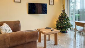 Ein Wohnzimmer mit braunem Ledersofa, einem Holztisch, einem Flachbildfernseher und einem Weihnachtsbaum.