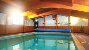 Piscina interna com paredes de madeira, borda azul e um banco.
