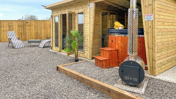 A wooden cabin with a hot tub, a patio with a chair and table, and a small garden area. - 2 bedroom accommodation in Barnard Castle (Barnard Castle)