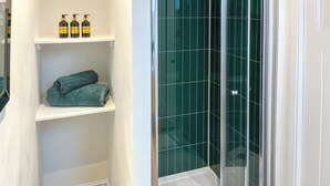 A bathroom with a glass shower enclosure, shelves with toiletries, and a green towel. - 2 bedroom accommodation in Barnard Castle (Barnard Castle)