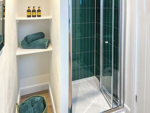 A bathroom with a glass shower enclosure, shelves with toiletries, and a green towel. - 2 bedroom accommodation in Barnard Castle (Barnard Castle)