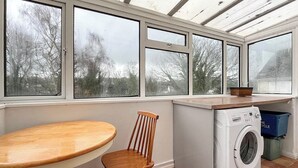 A compact kitchen with a washing machine, a wooden chair, a table, and large windows.