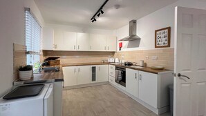 A modern kitchen with white cabinets, a stainless steel range hood, and a wooden countertop.