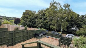 A fenced backyard with a patio area, gravel ground, and a view of a residential street with parked cars.