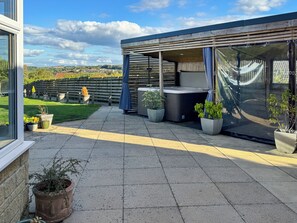 Ein überdachter Außenbereich mit Terrasse, Blumentöpfen und Blick ins Grüne.
