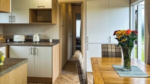 A compact kitchen with a dining area, wooden cabinets, a herringbone floor, and a view through a door. - 2 bedroom accommodation in Hartshorne (Hartshorne)