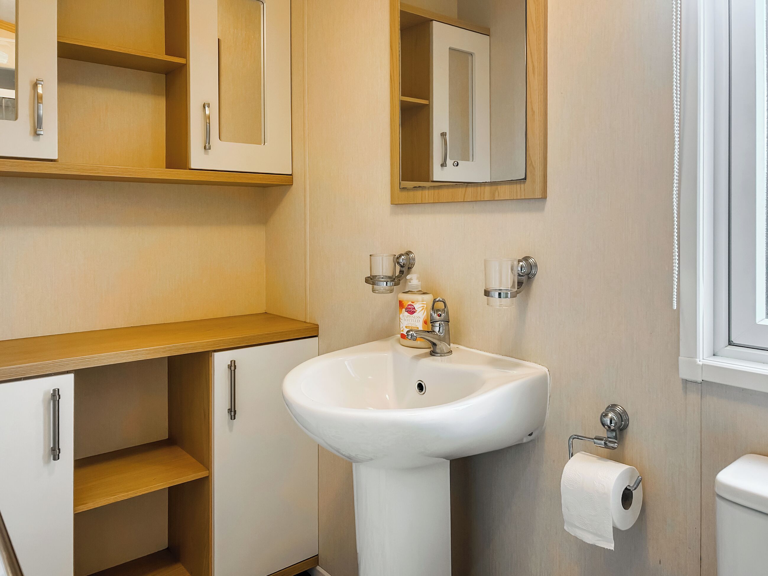A bathroom with a sink, mirror, toilet, and wooden cabinets.