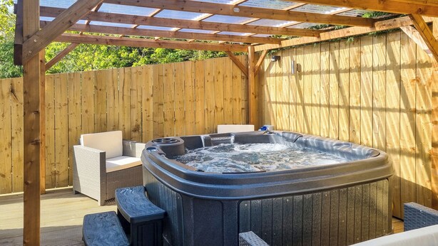 Un jacuzzi con asientos, rodeado de paneles de madera y una pérgola.