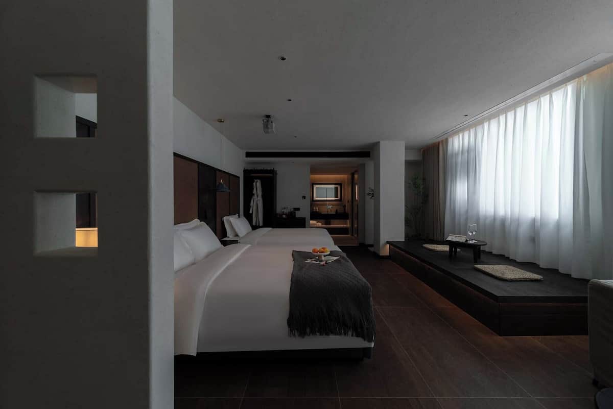 A modern hotel room with a large bed, a seating area with a table and chairs, and a TV in the background.