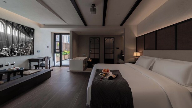 Una habitación de hotel moderna con una cama grande, un área de descanso con una mesa y sillas, una bañera y un ventanal con vistas al exterior.