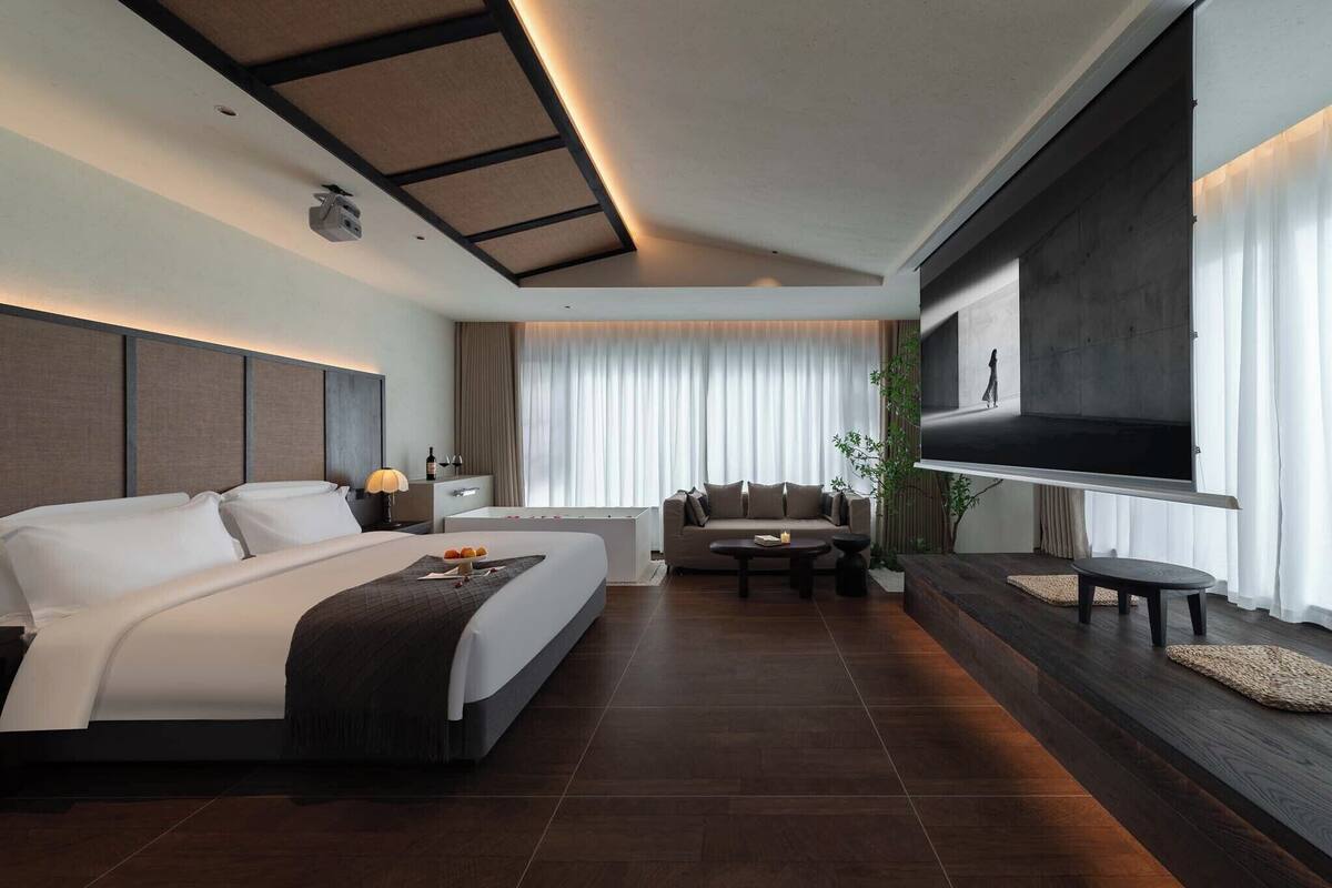 A modern hotel room with a large bed, a sofa, a TV, and a dining table.