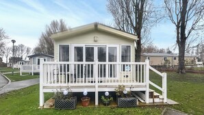Ein Bungalow mit weißem Veranda und kleiner Terrasse, umgeben von Gras und Bäumen.