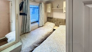 Ein Schlafzimmer mit zwei Betten, einem Fenster mit Vorhängen, einem kleinen Nachttisch und einem Kleiderschrank.