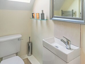 A bathroom with a toilet, a sink, a mirror, and a glass shelf with toiletries. - 1 bedroom accommodation in Bognor Regis, near Chichester (Bognor Regis)