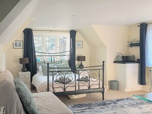 Une chambre à coucher comprenant un lit, des tables de chevet, une fenêtre avec des rideaux, un coin cuisine et une vue sur l’extérieur.
