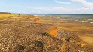 Eine Küstenlandschaft mit Kiesstrand, weiter Ferne und blauem Himmel.
