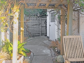 A wooden pergola over a narrow pathway leading to a white door, surrounded by potted plants and a wooden bench. - 1 bedroom accommodation in Bognor Regis, near Chichester (Bognor Regis)