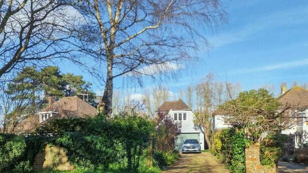 Eine Wohnstraße mit Häusern, einem geparkten Auto davor und einem wolkenlosen Himmel.