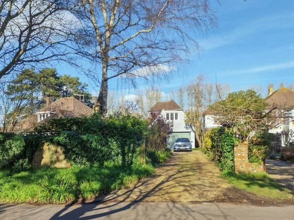 Eine Wohnstraße mit Häusern, einem geparkten Auto davor und einem wolkenlosen Himmel.