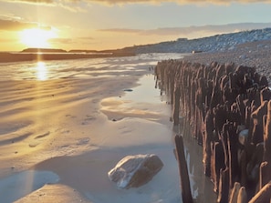 Une plage dont le rivage est gelé, avec un coucher de soleil en arrière-plan.